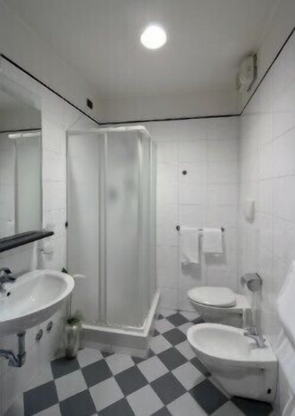 Un baño con ducha, dos lavamanos y un inodoro.