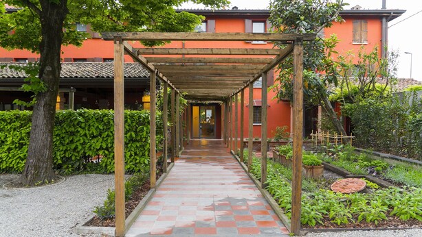 A covered walkway with a tiled floor leading to a building with orange walls and a tiled roof. - Antica Locanda Il Sole (Castel Maggiore)