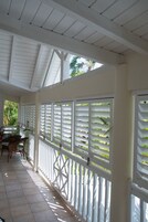 Eine überdachte Veranda mit weißen Geländern und Fliesenboden, mit einem Tisch und Stühlen.