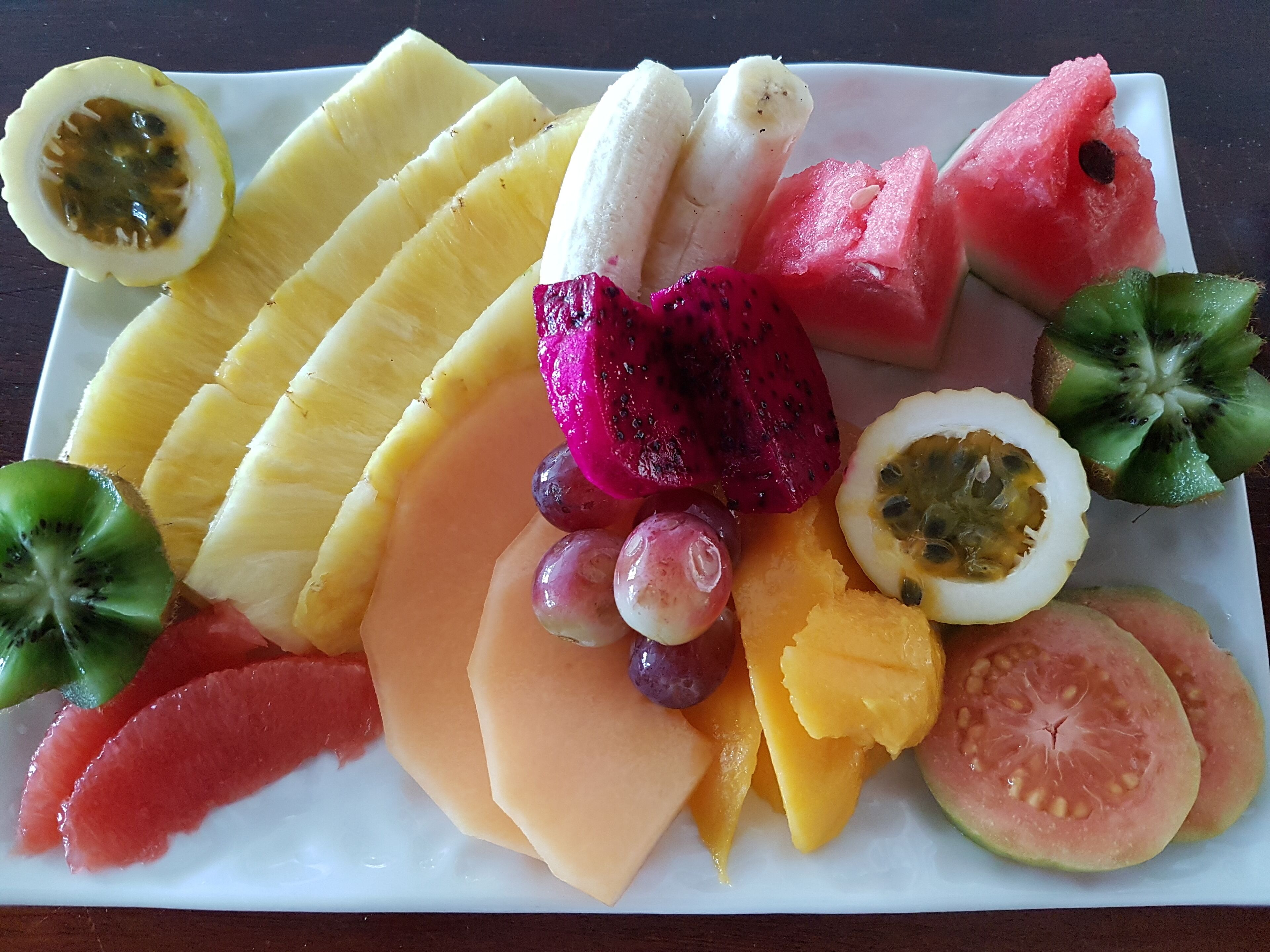 Un plato con frutas variadas como piña, plátano, sandía, kiwi, pitahaya, uvas y gajos de melón.