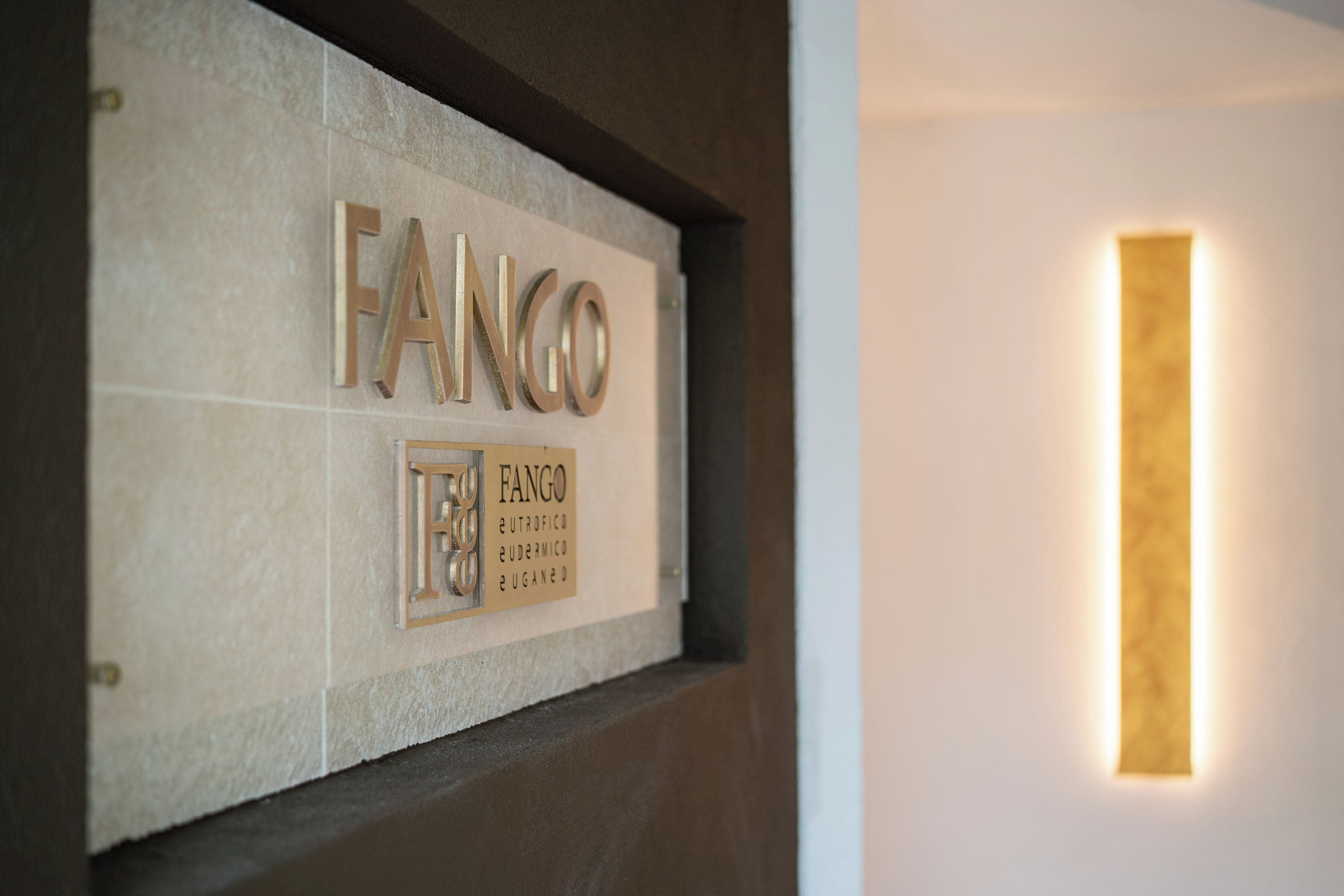 Un letrero montado en la pared con el nombre 'FANGO' y un letrero más pequeño debajo que enumera 'FANGO EUTROFICO EUDERMICO EUGANO'.