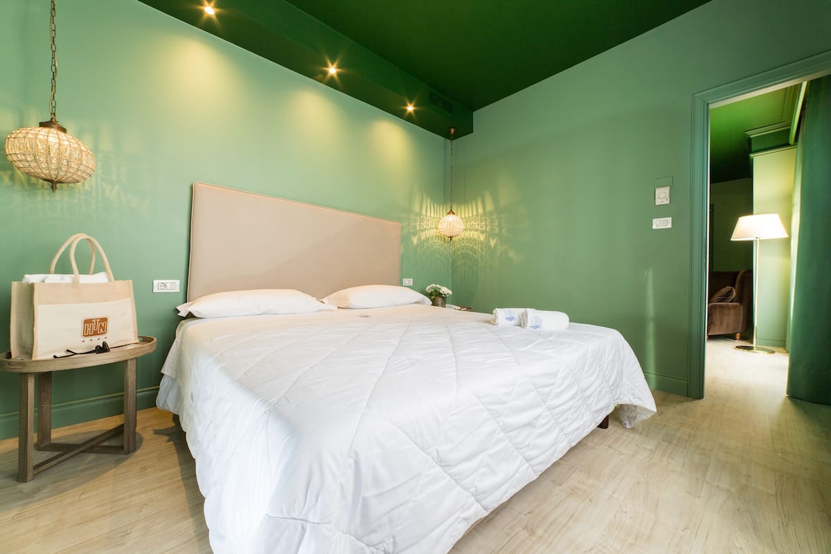Ein ordentlich bezogenes Bett in einem Zimmer mit grünen Wänden, Holzboden und einer Pendelleuchte.