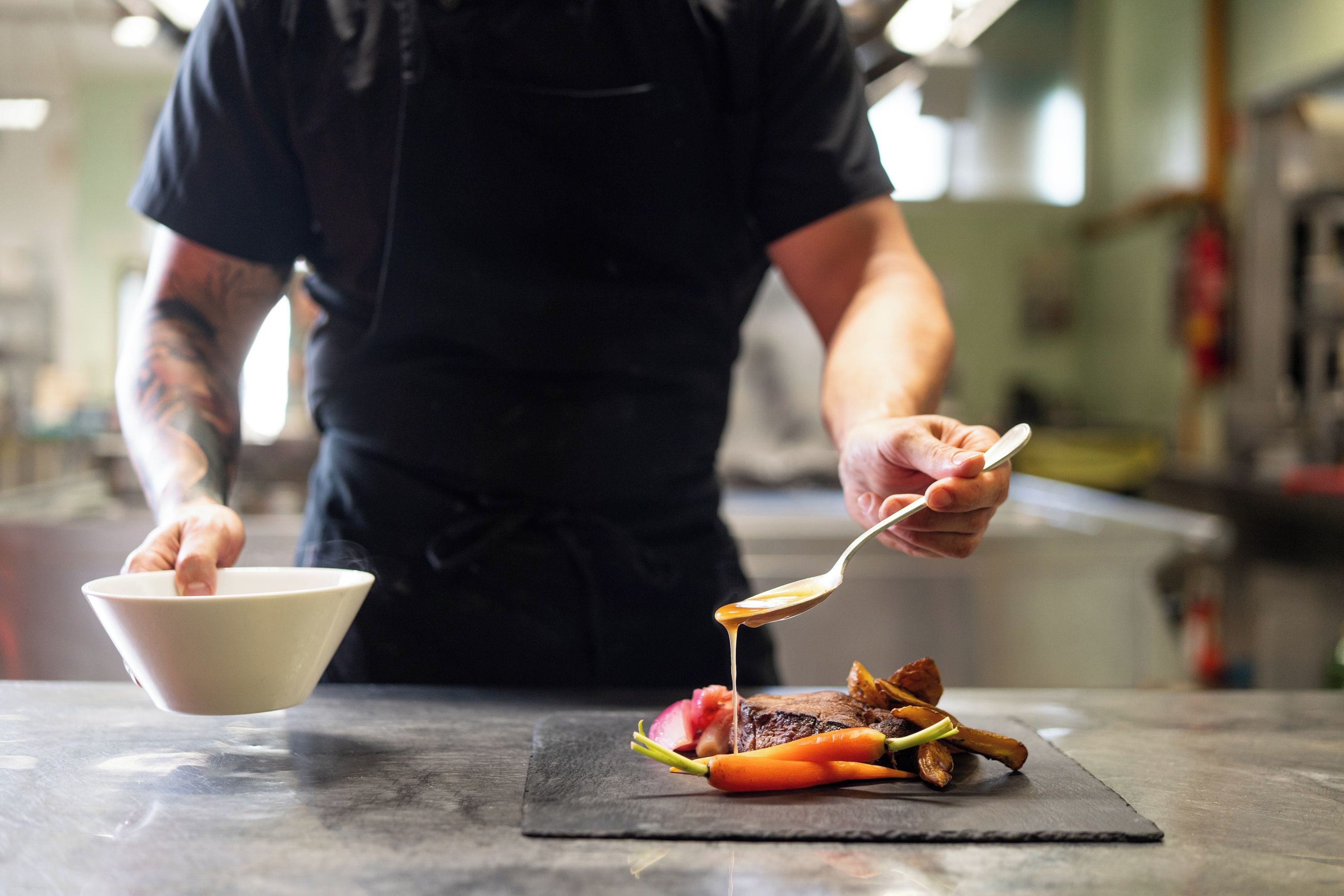 A person serving food on a slate board with a bowl and a spoon.