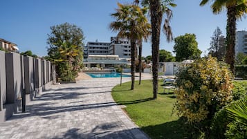 A paved walkway leading to a pool area with palm trees and a building in the background.