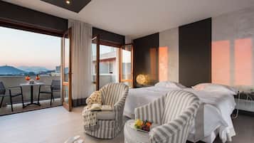 A hotel room with a bed, two armchairs, a small table, and a balcony with a view of the city.