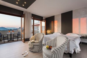 Habitación de hotel con cama, dos sillones, una mesita y un balcón con vistas a la ciudad.