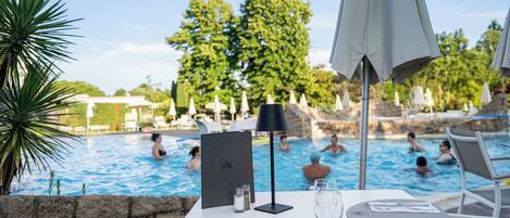 Mesa junto a la piscina con un menú, saleros y pimenteros, un vaso de agua y una lámpara negra.