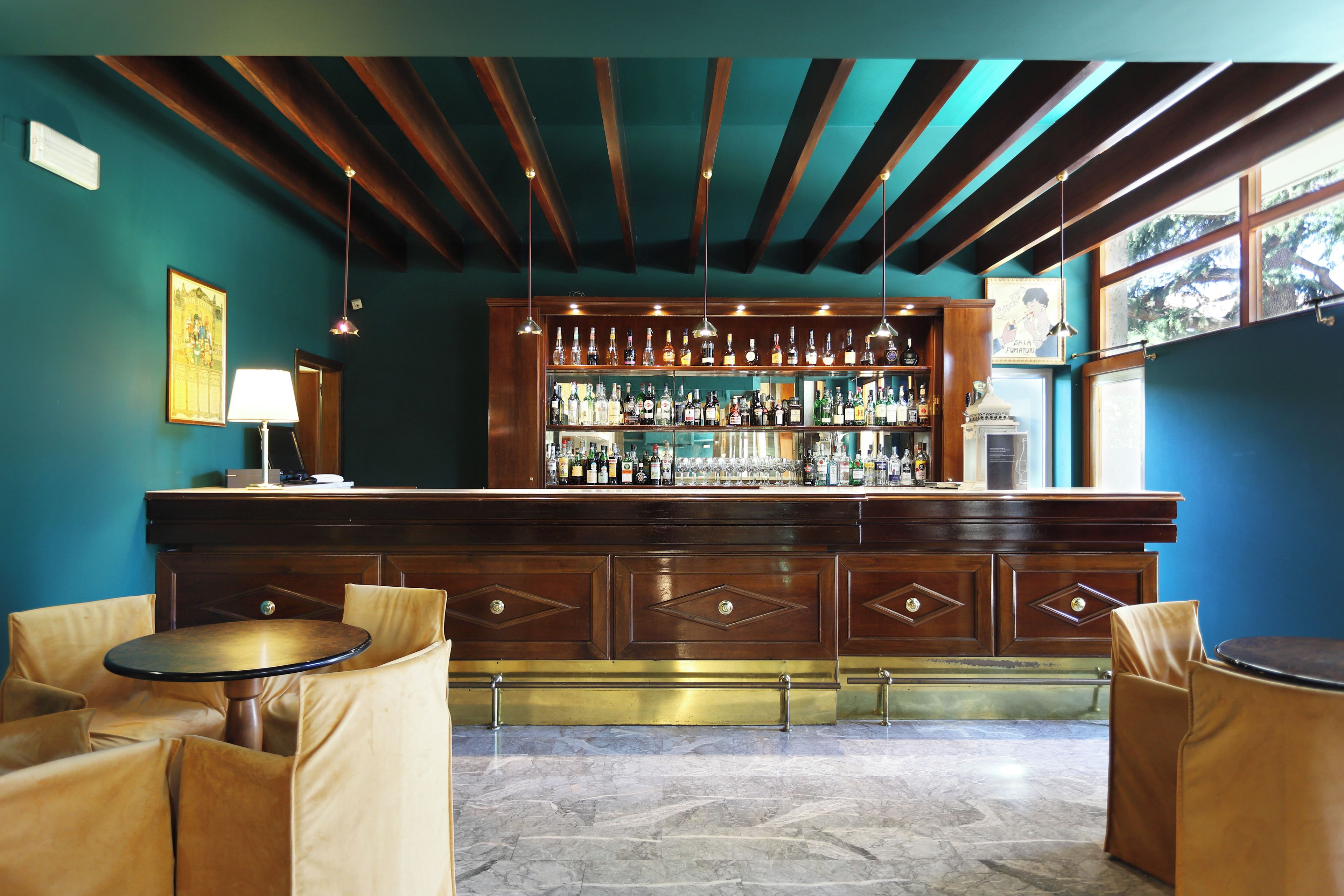 A bar area with a wooden counter, shelves of bottles, hanging lights, and cushioned seating.