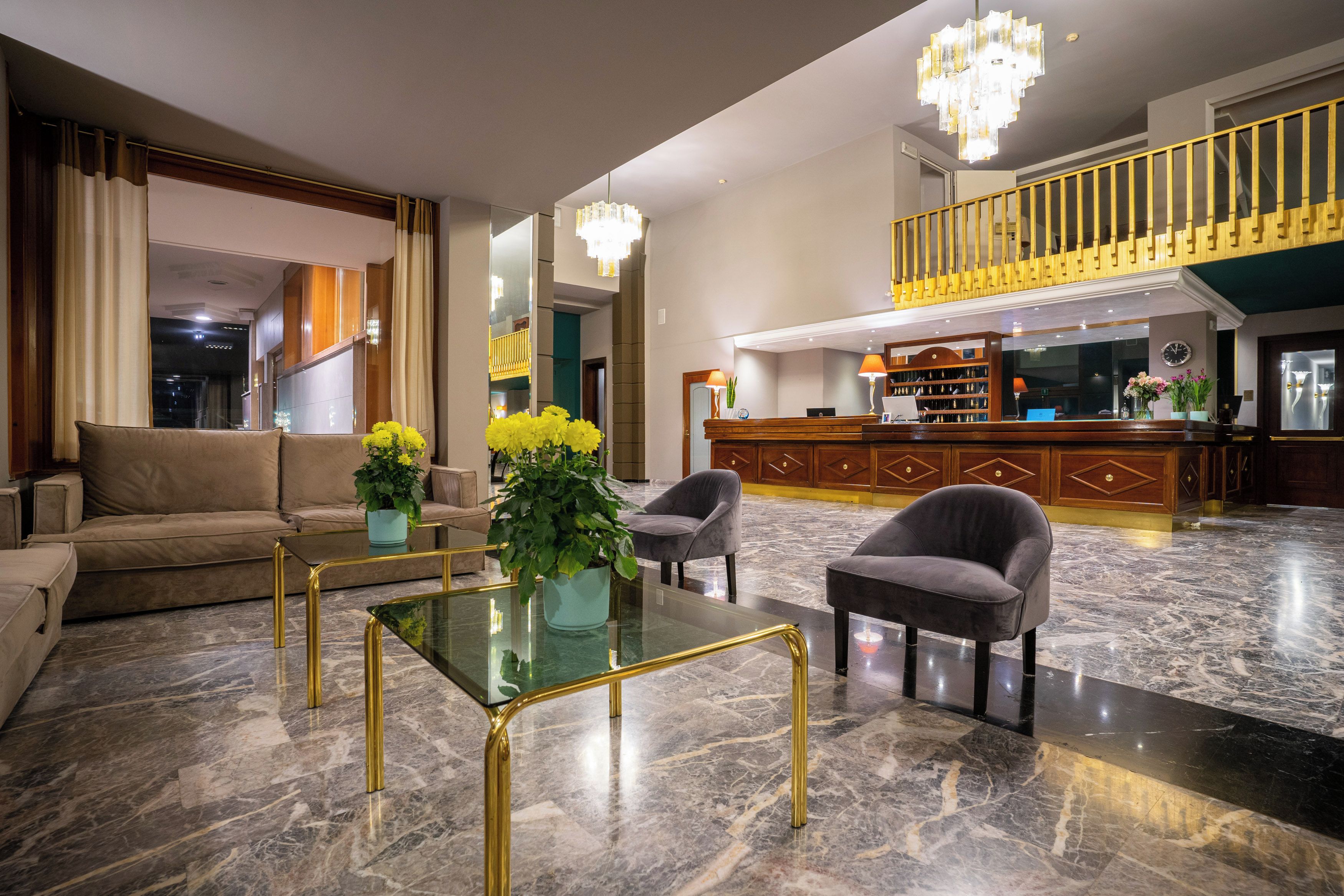 Eine großzügige Lobby mit Marmorboden, einer Rezeption, einer Treppe und einer Sitzecke mit Sofa und Sesseln.