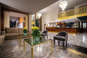 Un vestíbulo amplio con piso de mármol, una recepción, una escalera y un área de descanso con sofá y sillones.