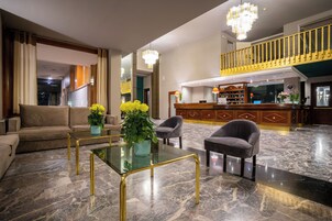 Un vestíbulo amplio con piso de mármol, una recepción, una escalera y un área de descanso con sofá y sillones.