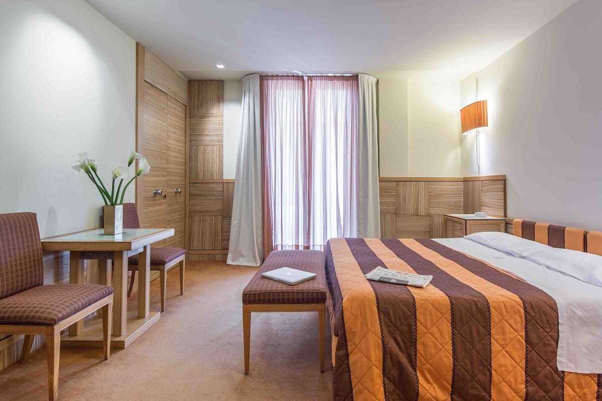 Ein Hotelzimmer mit einem Bett, einem Schreibtisch mit einem Laptop, einem Stuhl und einem Nachttisch.