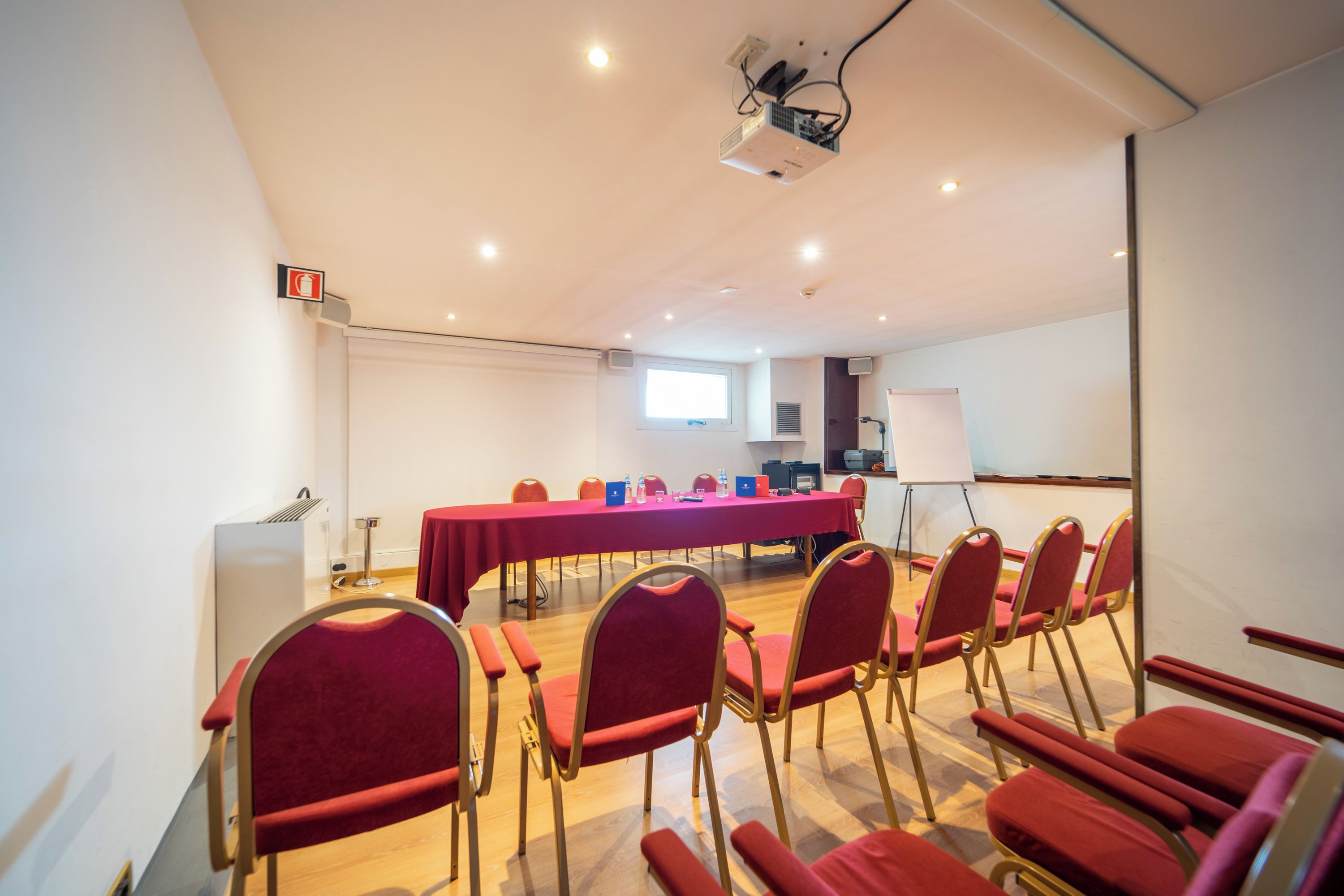 A conference room with a long table, red chairs, a projector, and a whiteboard.