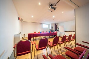 Un salón de conferencias con una larga mesa, sillas rojas, un proyector y una pizarra.
