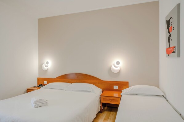 A hotel room with two beds, a wooden headboard, bedside tables, and wall-mounted light fixtures. - Nuova Barcaccia (Peschiera del Garda)
