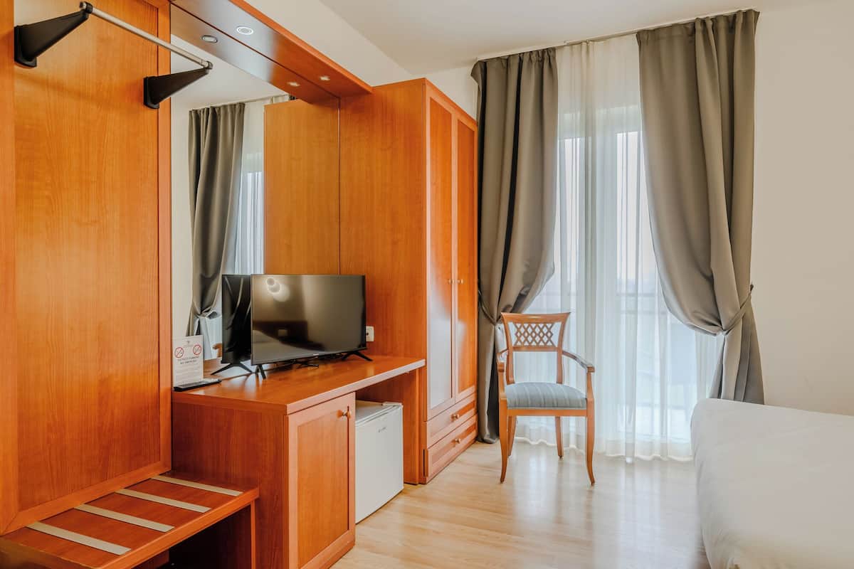 Ein Hotelzimmer mit einem Holzschrank, einem Fernseher auf einem Tisch, einem Sessel und einem Bett.