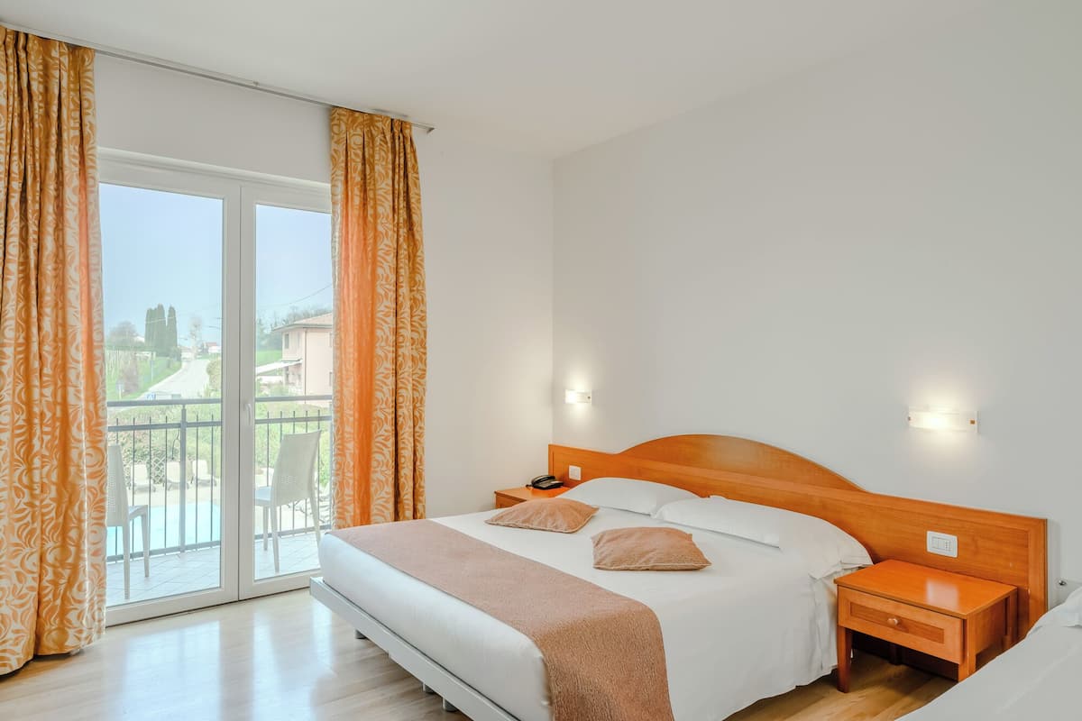 Ein Hotelzimmer mit Bett, Nachttischen und Blick auf einen Balkon mit Vorhängen.