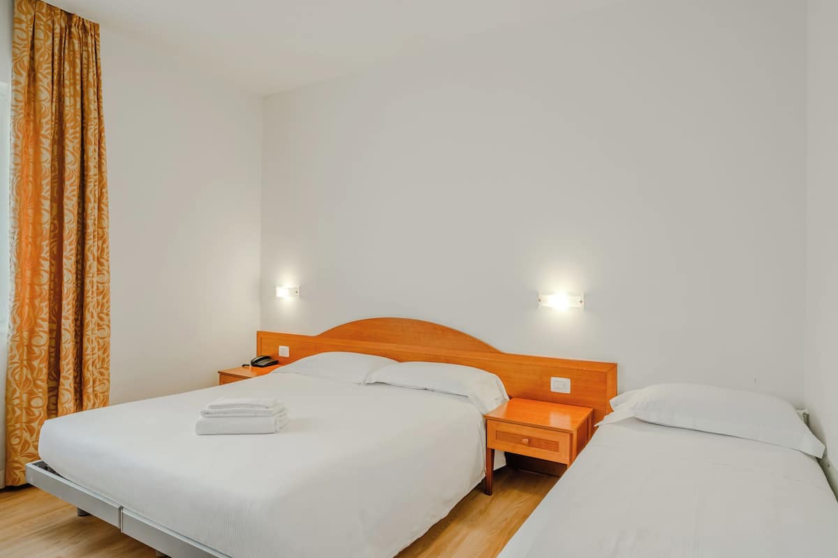 Ein Hotelzimmer mit zwei Einzelbetten, Holz-Kopfteilen, Nachttischen mit Lampen und einem Vorhang mit Blumenmuster.