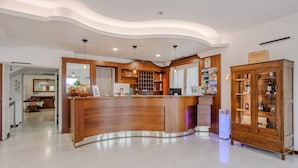 A reception area with a curved wooden counter, a reception desk, a mirror, and a wooden cabinet with glass doors. - Nuova Barcaccia (Peschiera del Garda)