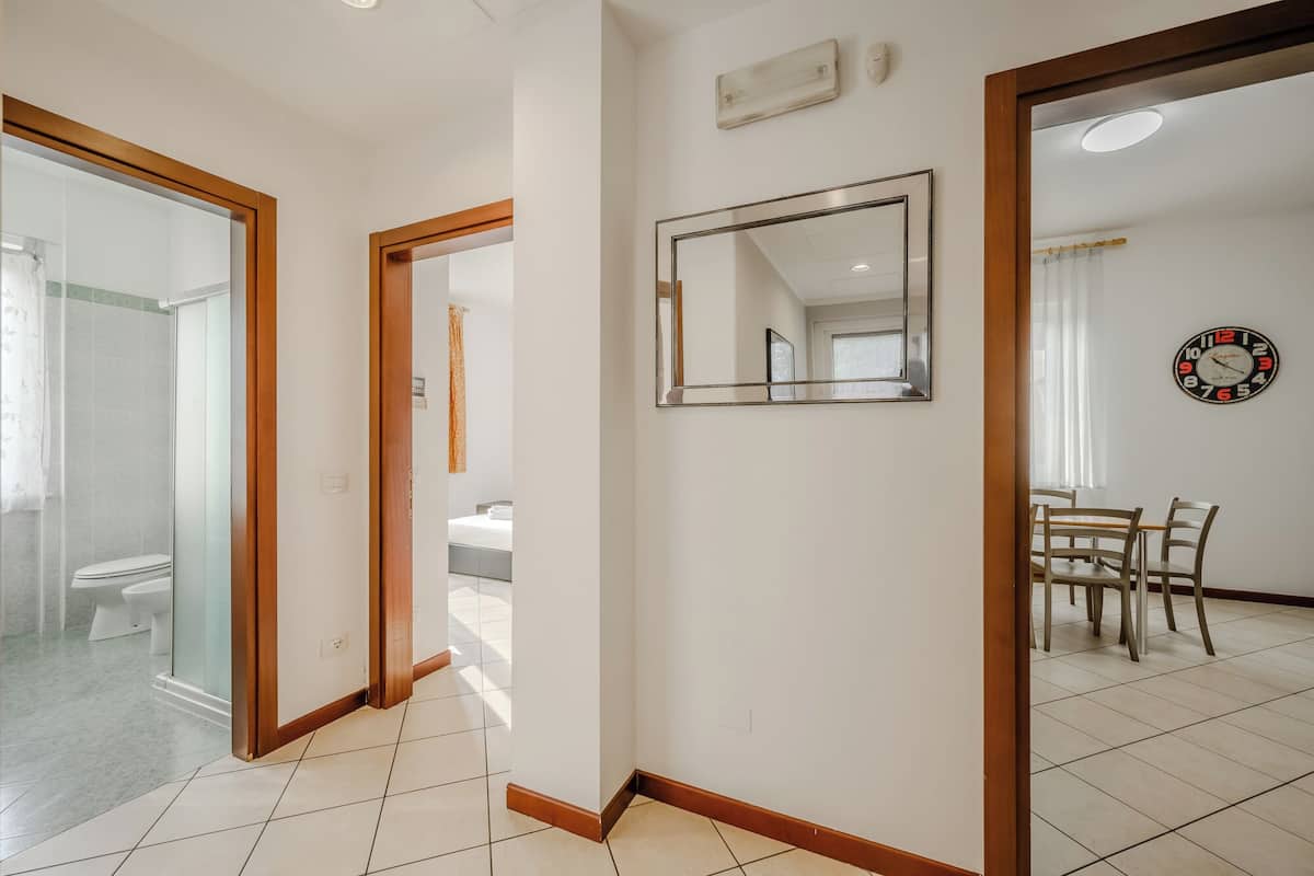 Ein Hotelzimmer mit Glasdusche, Holztür, Spiegel und einem Essbereich mit Tisch und Stühlen.