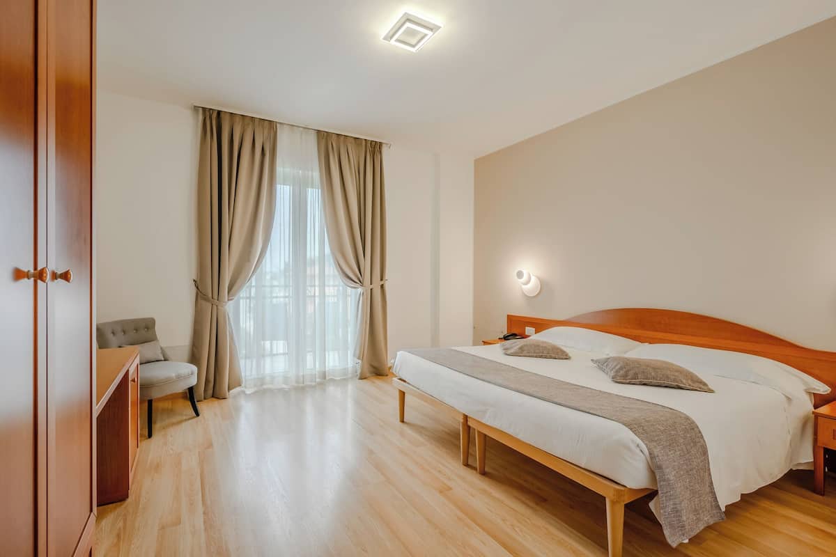Ein Schlafzimmer mit einem hölzernen Bett, einem Nachttisch, einem Stuhl und einem Fenster mit Vorhängen.
