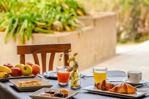 A breakfast setting with fruits, pastries, juice, and coffee on a table outdoors.