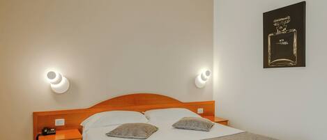 A neatly arranged bedroom with a wooden bed, two bedside tables, and a wall-mounted lamp.