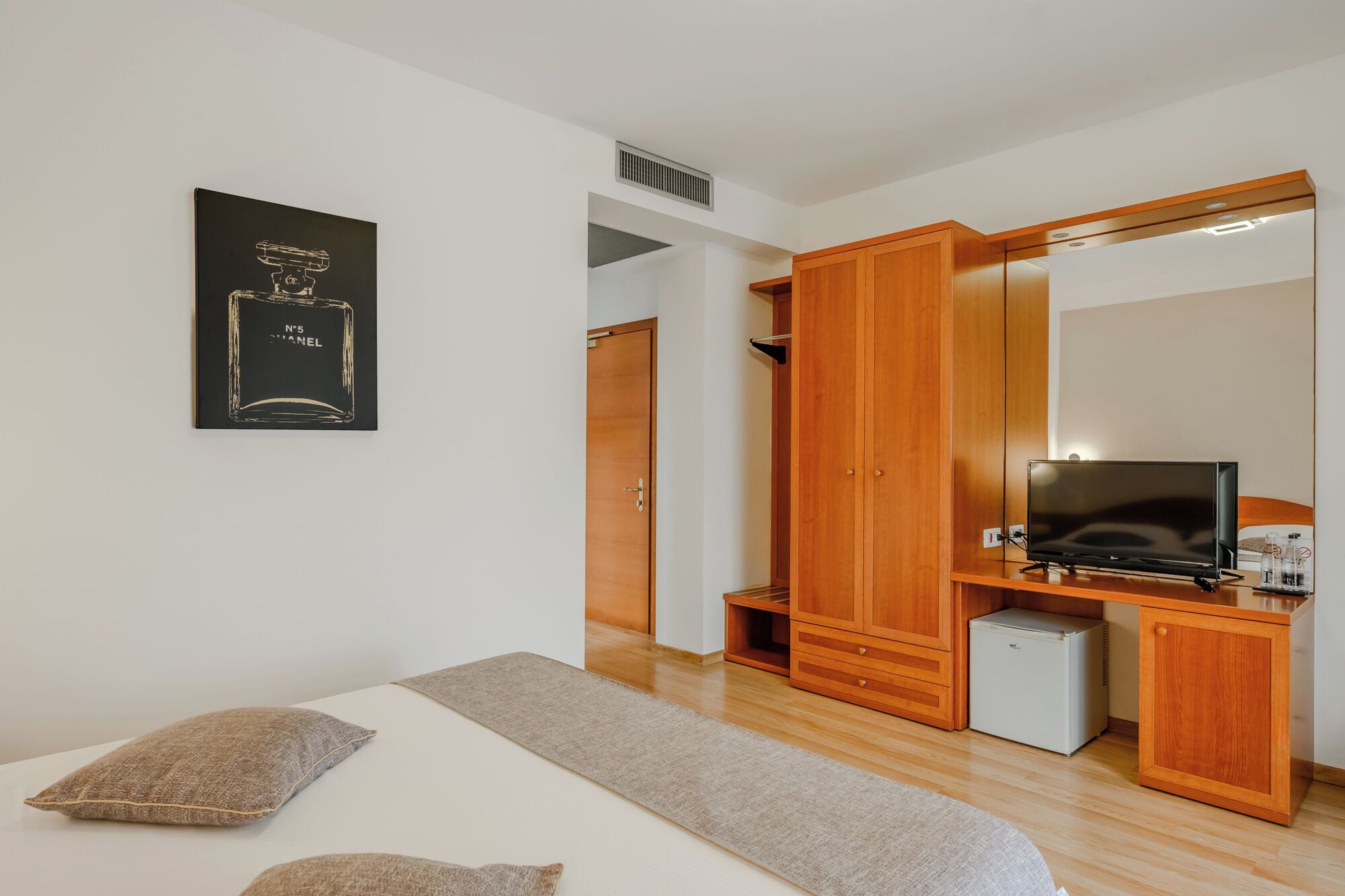 Een slaapkamer met een bed, een kledingkast, een televisie en een kleine koelkast.