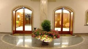 A lobby with two arched doorways leading to rooms, a marble floor, and a central floral arrangement. - Capys (Capua)