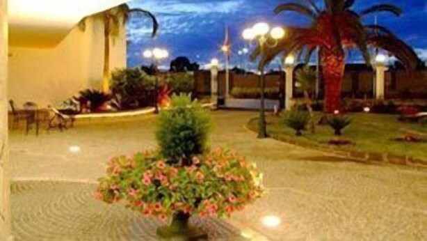 A courtyard with a palm tree, a flower bed, and a building with a balcony. - Capys (Capua)