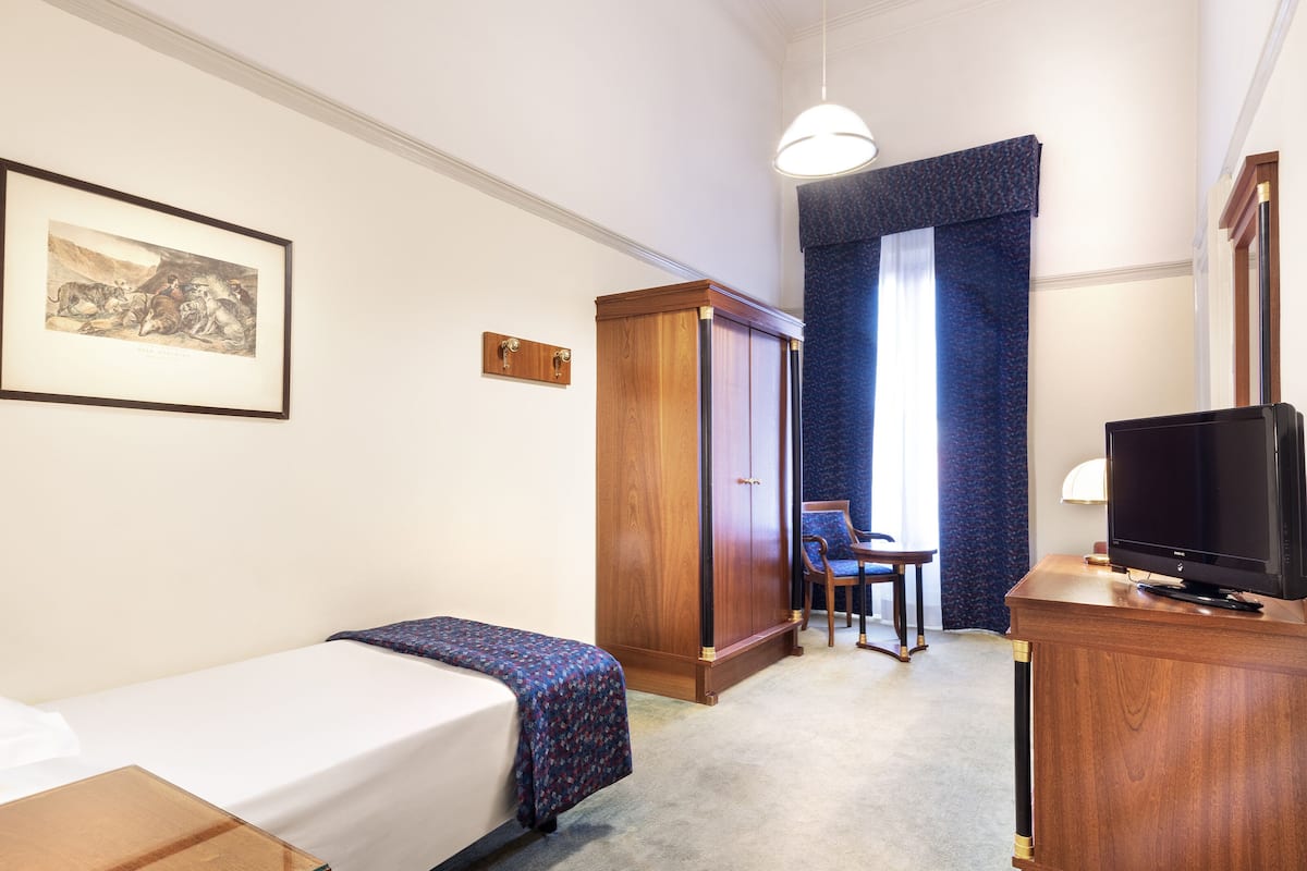 A hotel room with a single bed, a desk with a television, a wardrobe, and a chair.