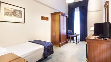 Una habitación de hotel con una cama individual, un escritorio con televisor, un armario y una silla.