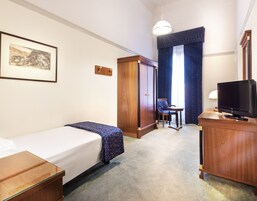 Una habitación de hotel con una cama individual, un escritorio con televisor, un armario y una silla.
