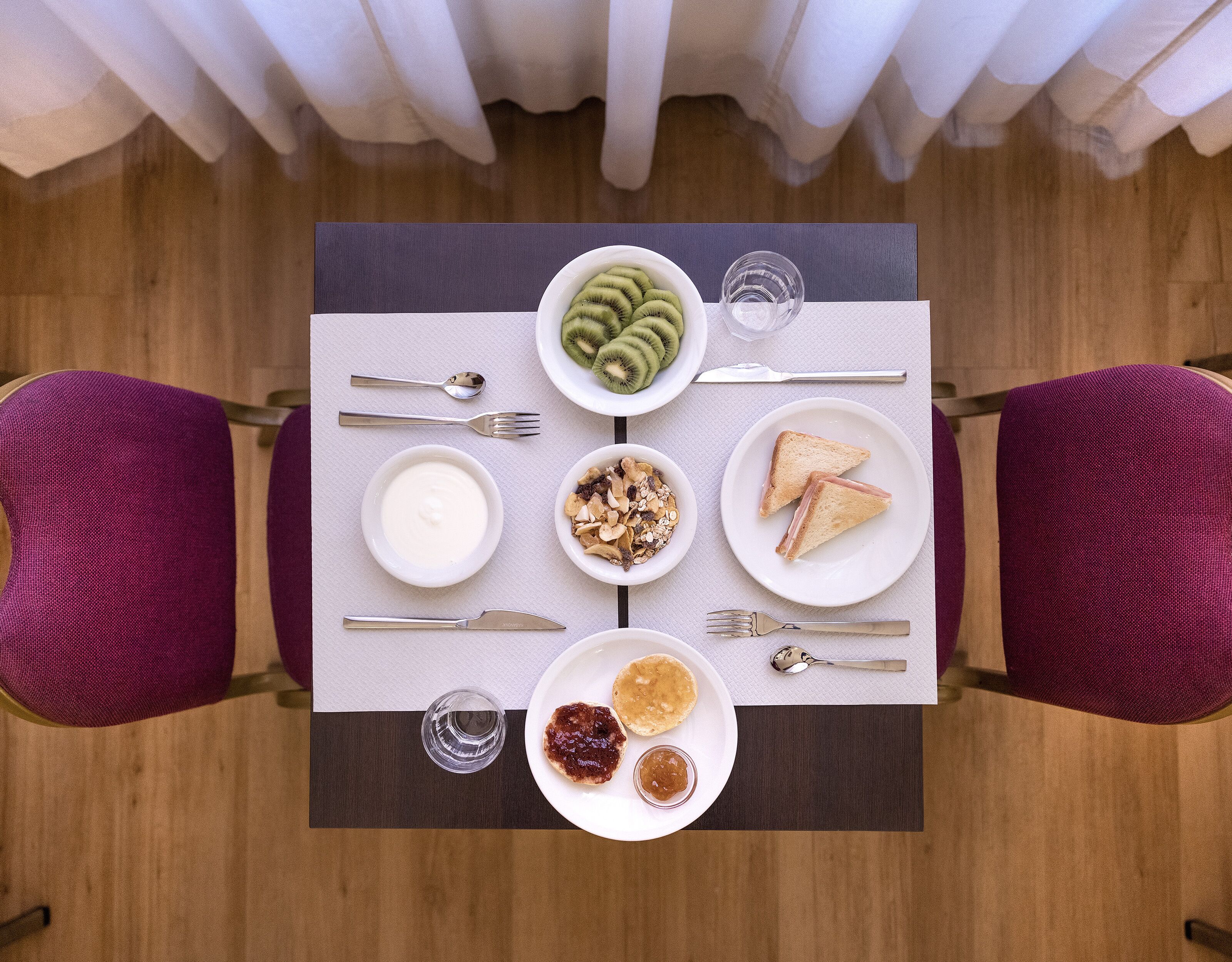 Een ontbijttafel met yoghurt, granola, toast en een bord met kiwischijfjes.