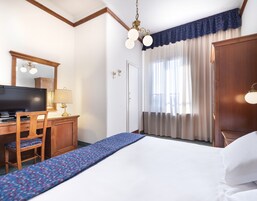 A hotel room with a bed, a desk with a television, a chair, and a wardrobe.