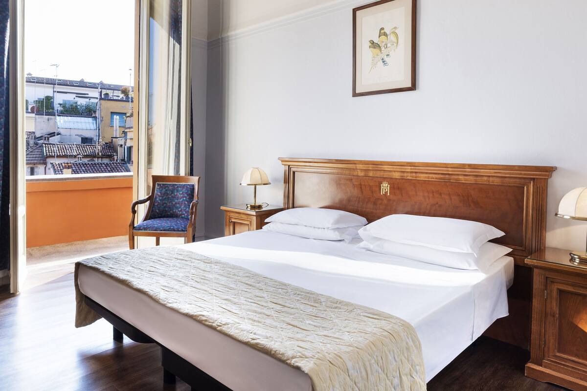 A hotel room with a large bed, a chair, a bedside table with a lamp, and a framed picture on the wall.