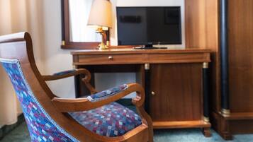 A wooden chair with a patterned cushion, a desk with a television, and a mirror on the wall.