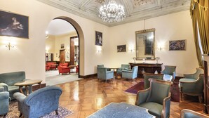 A spacious lobby with a high ceiling, ornate ceiling design, and a chandelier. There are multiple seating areas with chairs and tables. - Hotel Palace Bologna Centro (Bologna)