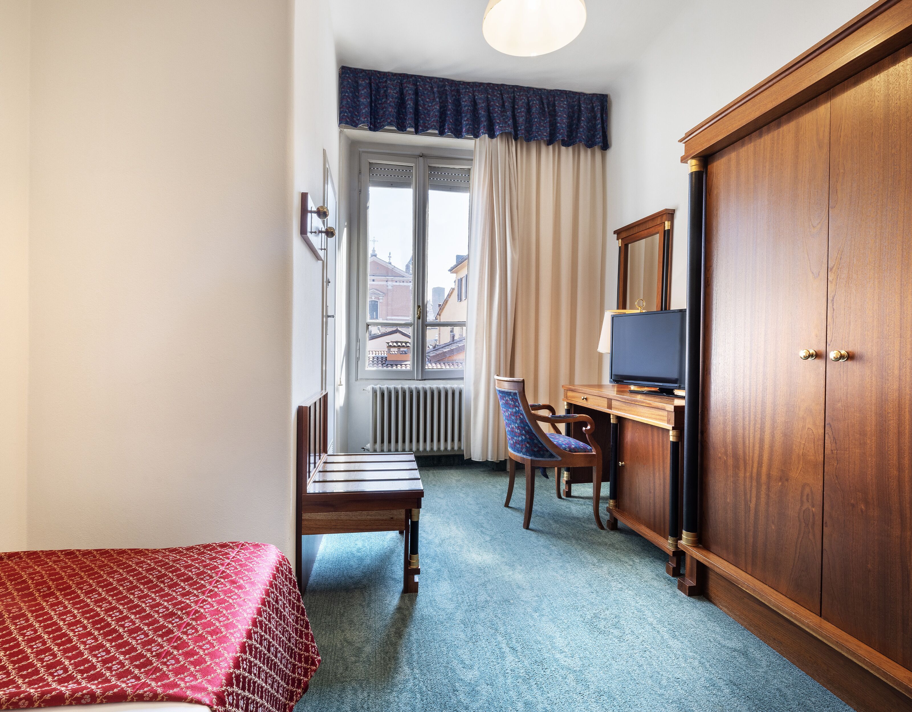 Une chambre d’hôtel comprenant un lit, un bureau avec une télévision, une chaise et une armoire.
