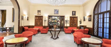 A spacious lobby with a grand chandelier, red upholstered chairs, and a central table.