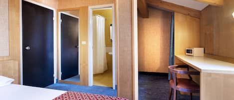 A hotel room with a bed, a desk, and a shower area.