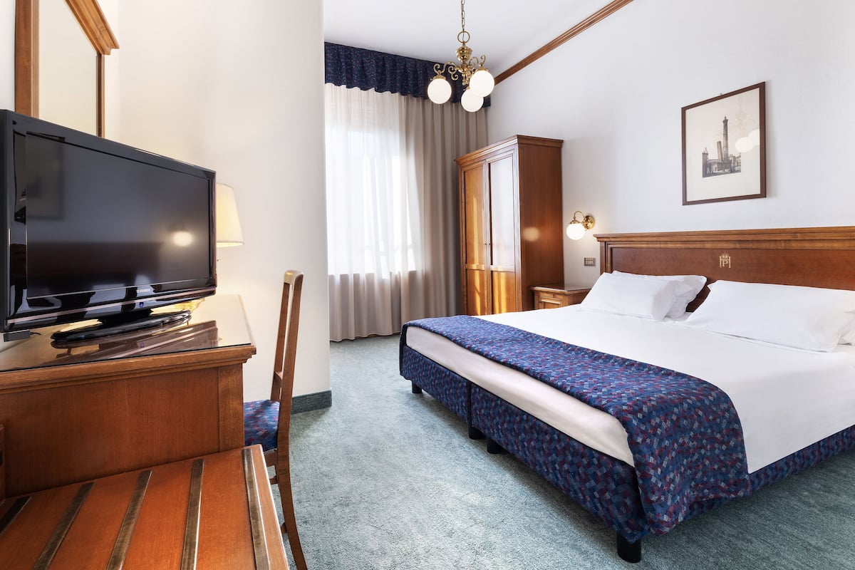 A hotel room with a bed, a TV, a desk, and a chair.