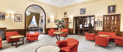 Vestíbulo de hotel con sillones rojos, una araña y un espejo grande.