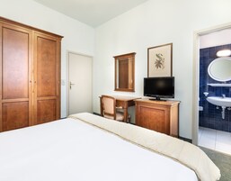 Una camera d'albergo con un letto, una scrivania con una sedia, una televisione, un quadro incorniciato e un bagno con lavandino e specchio.