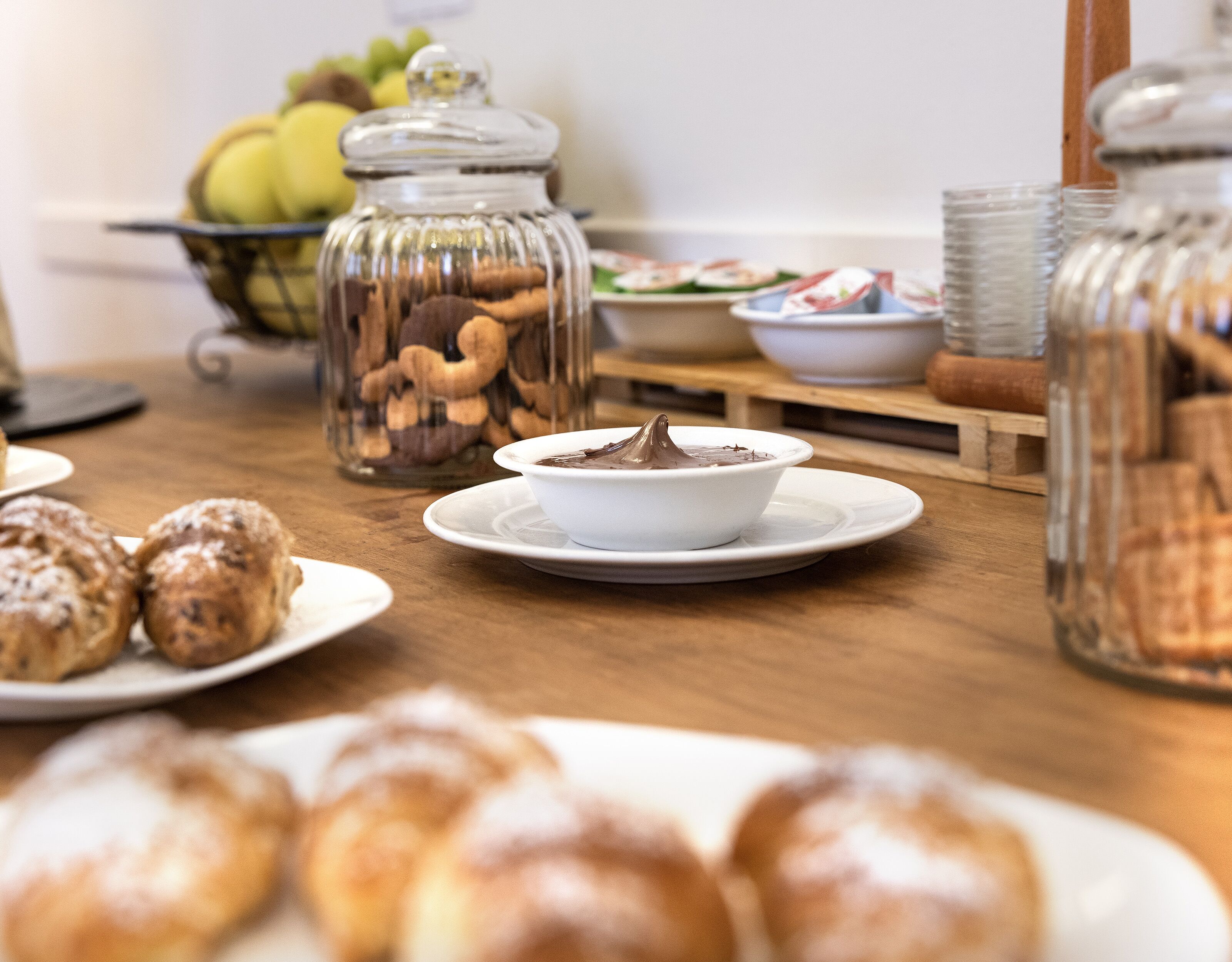 A table with a bowl of chocolate mousse, pastries, and jars of nuts.