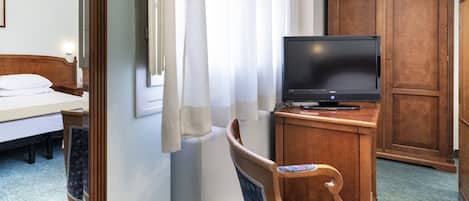 A hotel room with a bed, a television on a wooden cabinet, a chair with a patterned cushion, and a wardrobe.