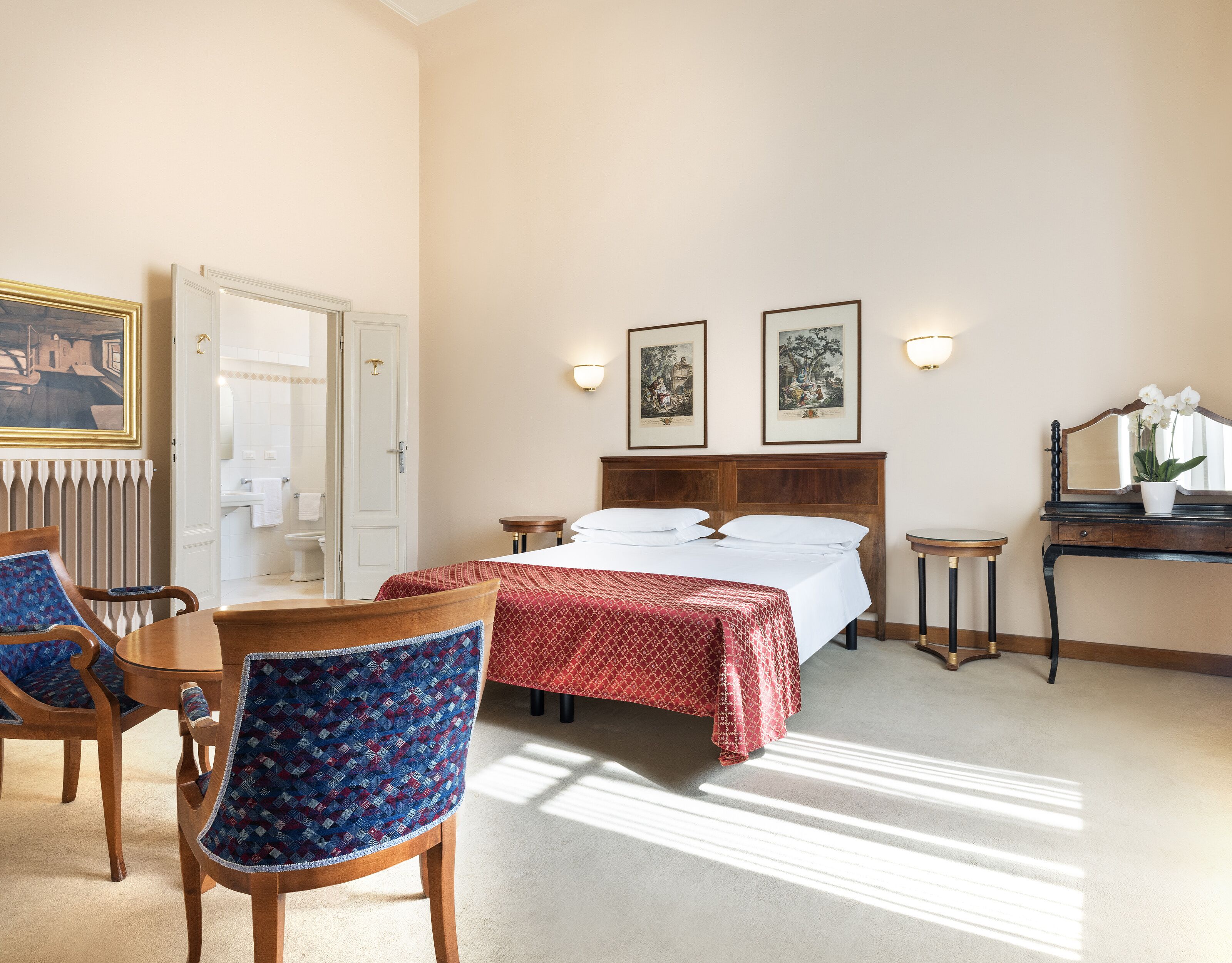 Een hotelkamer met een bed, twee nachtkastjes, een stoel, een kleintje tafeltje en een spiegel.