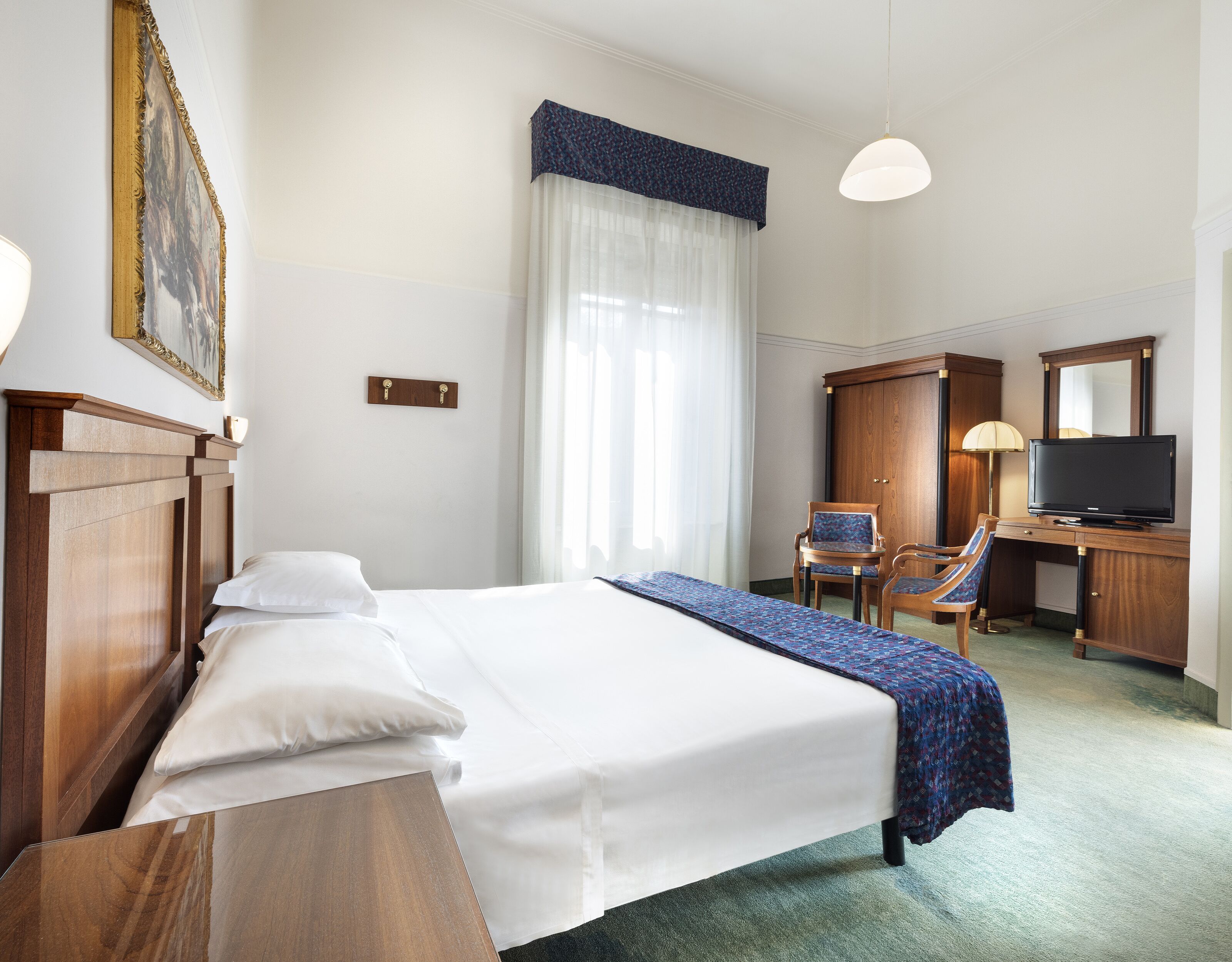A hotel room with a bed, a desk, a chair, a television, and a large window with curtains.