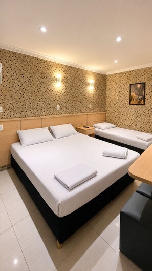 A hotel room with two beds, a small table, and a wall-mounted light fixture.