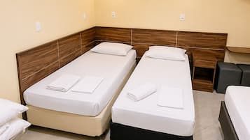 A hotel room with two single beds, a flat-screen TV mounted on the wall, and a small bedside table with a lamp.
